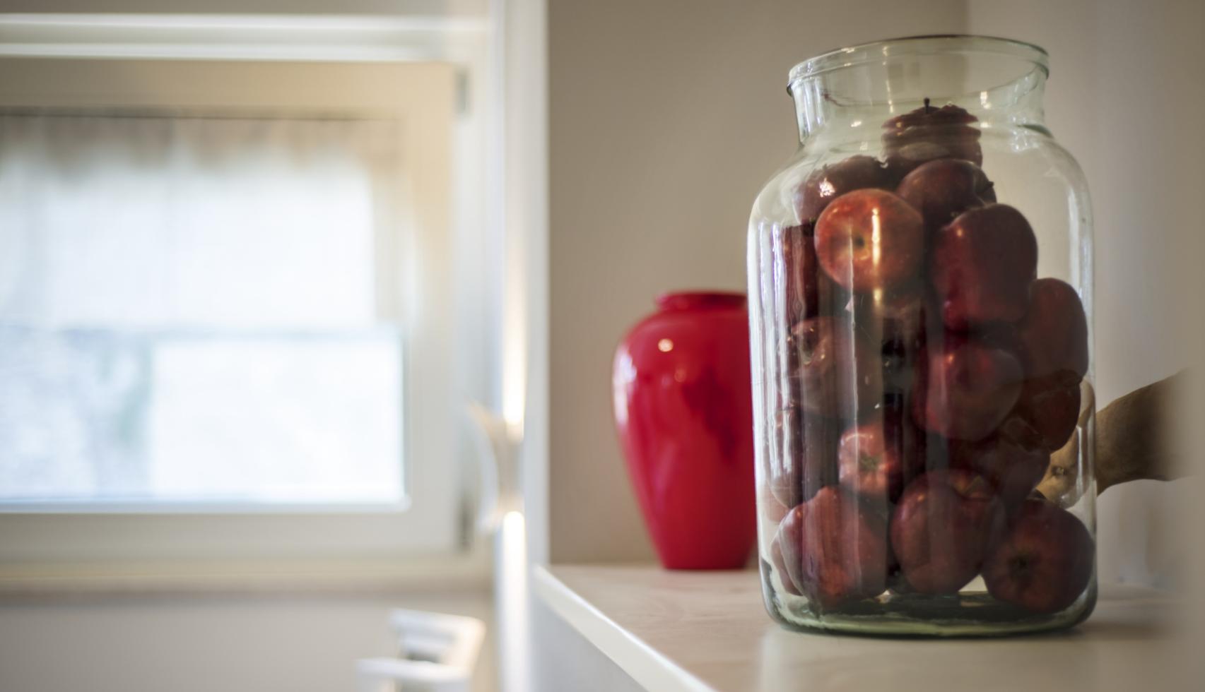 Glass jar with red apples on a shelf.