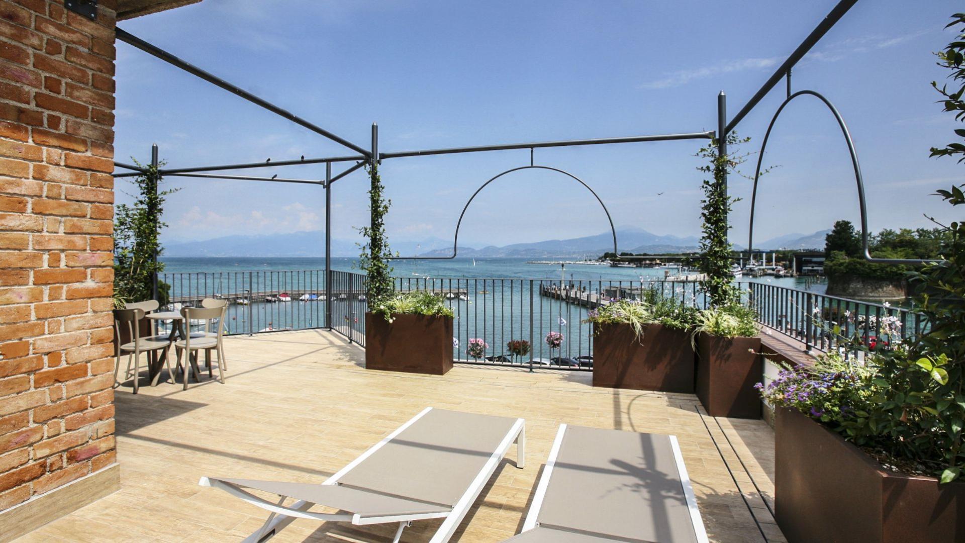 Terrazza con vista lago, arredi moderni e piante, cielo sereno e rilassante.