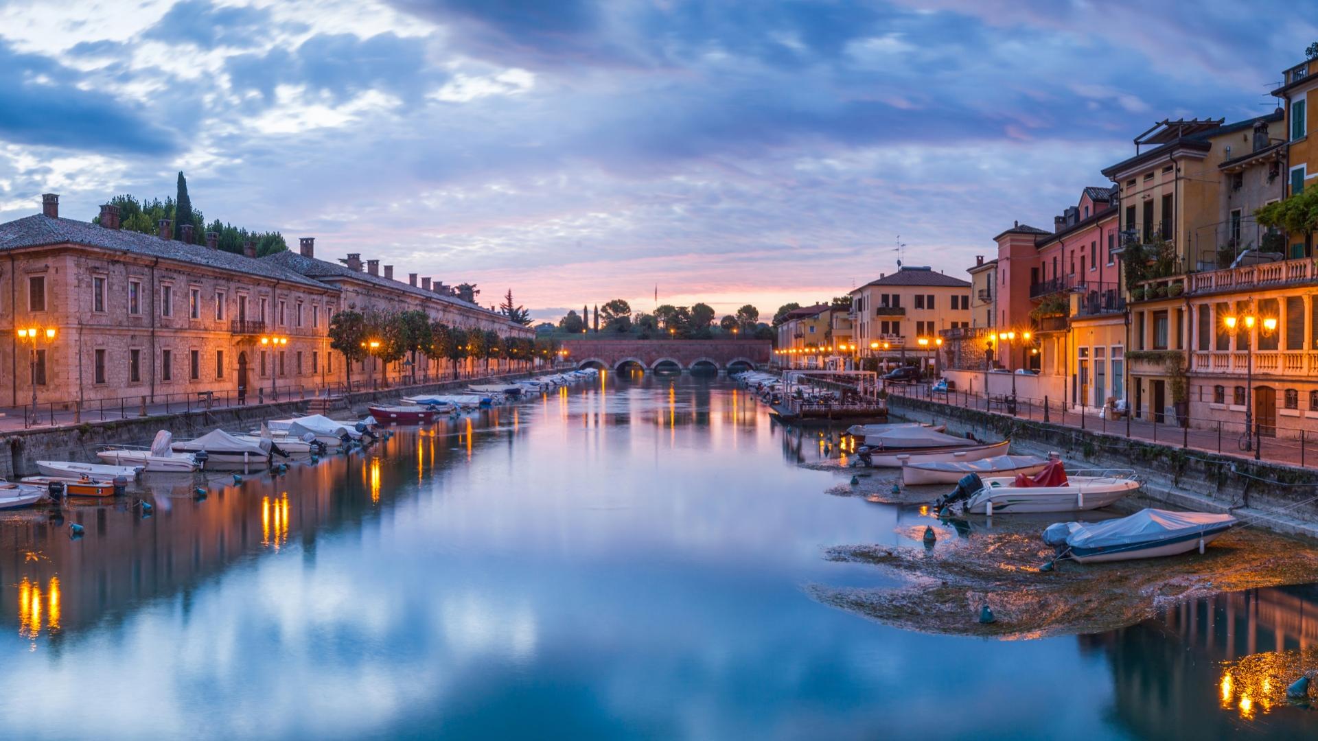 Tramonto sul canale con barche e edifici storici, atmosfera serena e luminosa.