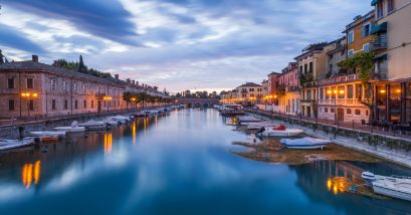 Tramonto su canale con barche, edifici storici e cielo nuvoloso.