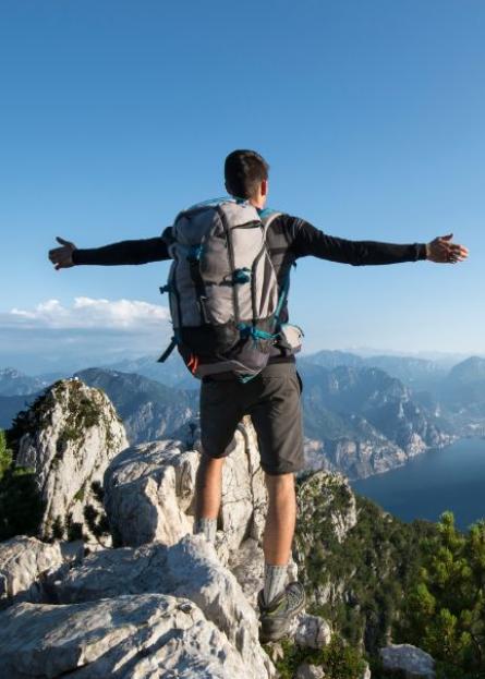 Escursionista con zaino ammira il panorama montano da una vetta rocciosa.