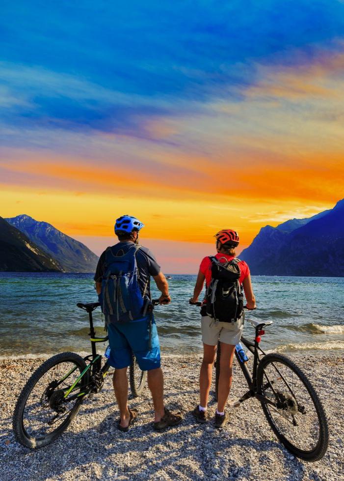 Due ciclisti ammirano il tramonto su una spiaggia di montagna.