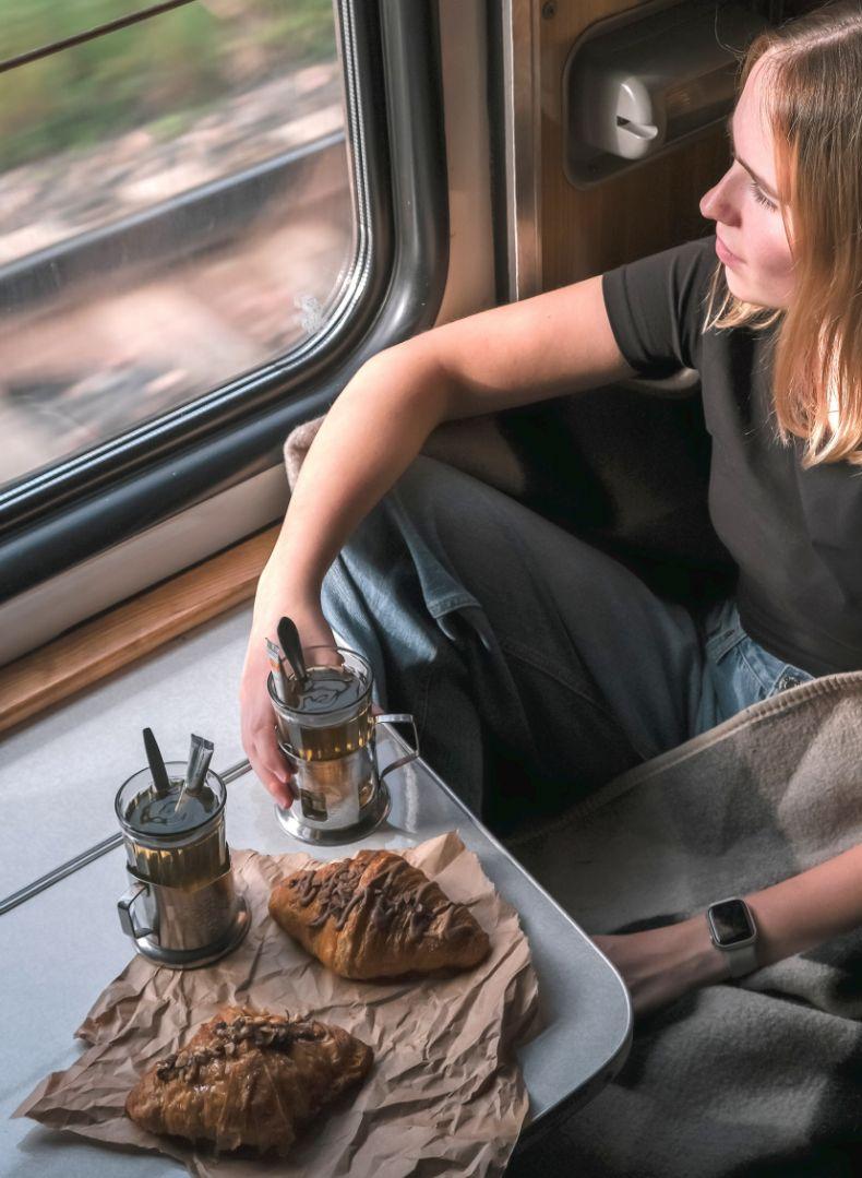 Donna su un treno, con tè e croissant, guarda fuori dal finestrino.